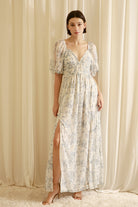Woman wearing a floral dress with a slit in front against a beige curtain background