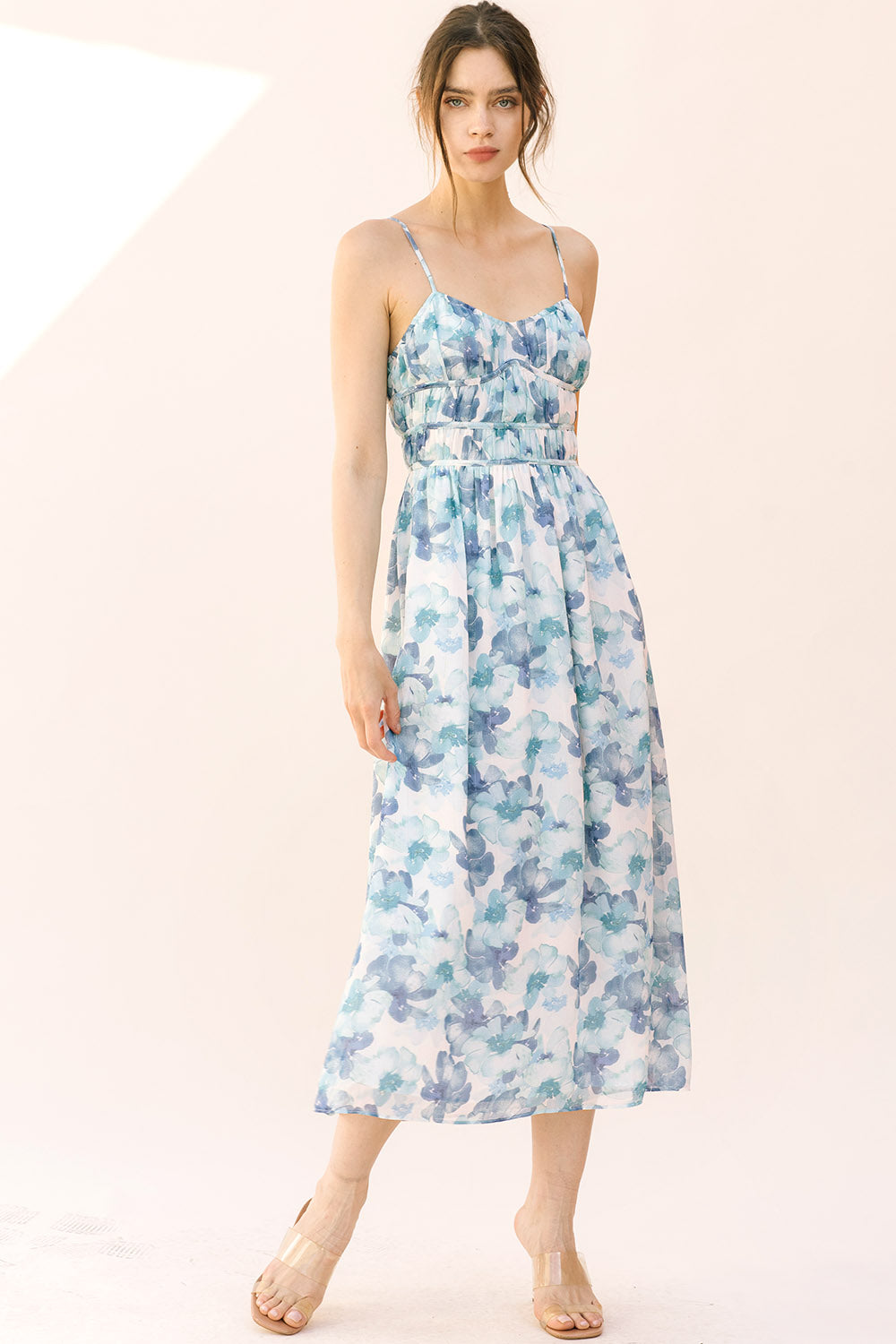 Woman wearing a blue floral midi dress with thin straps on a plain background