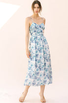 Woman wearing a blue floral midi dress with thin straps on a plain background