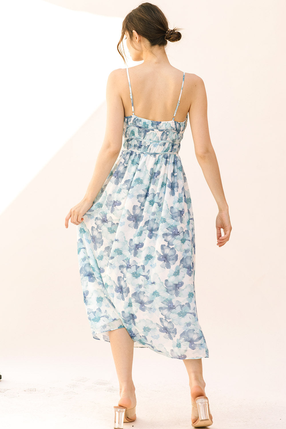 Back view of a woman wearing a blue watercolor floral midi dress on a plain background