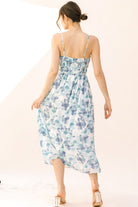 Back view of a woman wearing a blue watercolor floral midi dress on a plain background