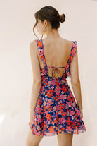 Back view of a woman wearing a colorful floral dress against a plain background