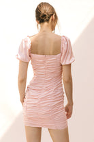 Back view of a woman wearing a pink dress with sheer panels on a light background