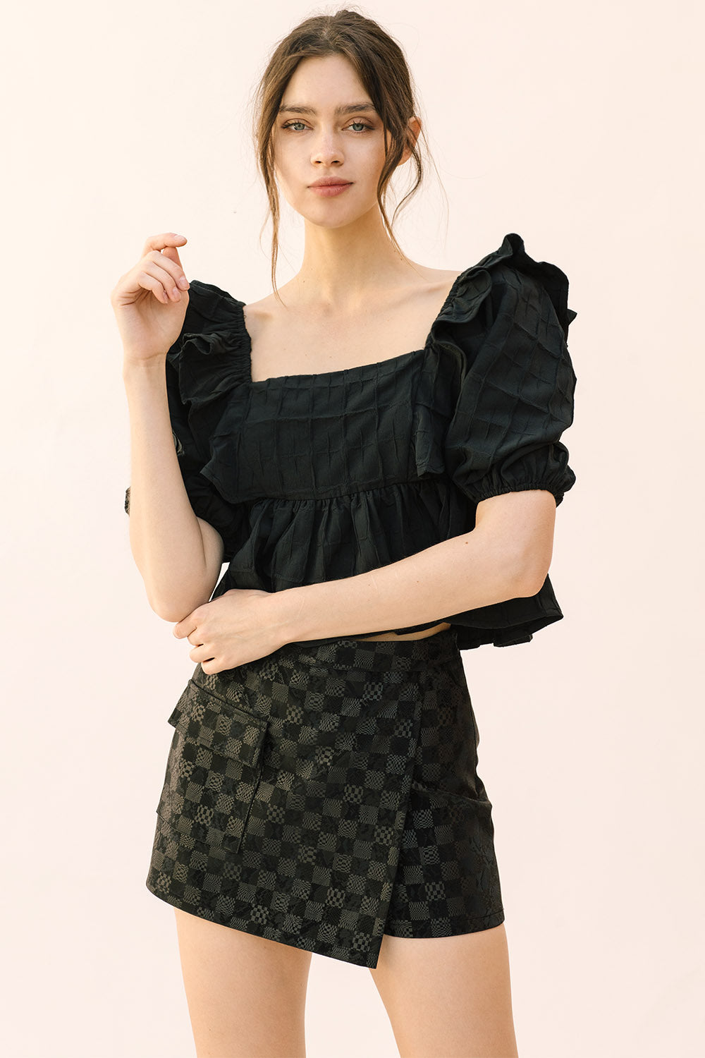 Woman wearing a black top and patterned shorts on a beige background