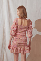 Back view of a woman wearing a pink floral dress against a plain background