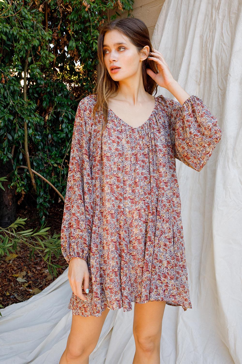 Woman wearing a floral dress standing outdoors with greenery in the background