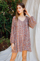 Woman wearing a floral dress standing outdoors with greenery in the background