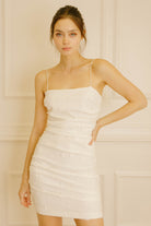 Woman wearing an ivory bodycon mini dress against a beige wall.