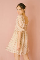 Back view of a woman wearing a beige polka dot dress against a pink background