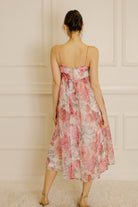 Back view of a woman wearing a large floral print midi dress against a neutral wall