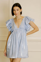 Woman wearing a light blue dress with ruffled sleeves against a neutral background
