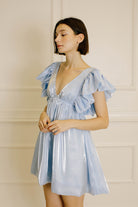 Side view of a woman wearing a light blue dress with ruffled sleeves against a neutral background