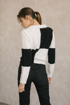 Back view of a woman wearing a black and white checkered zip-up sweater against a beige background
