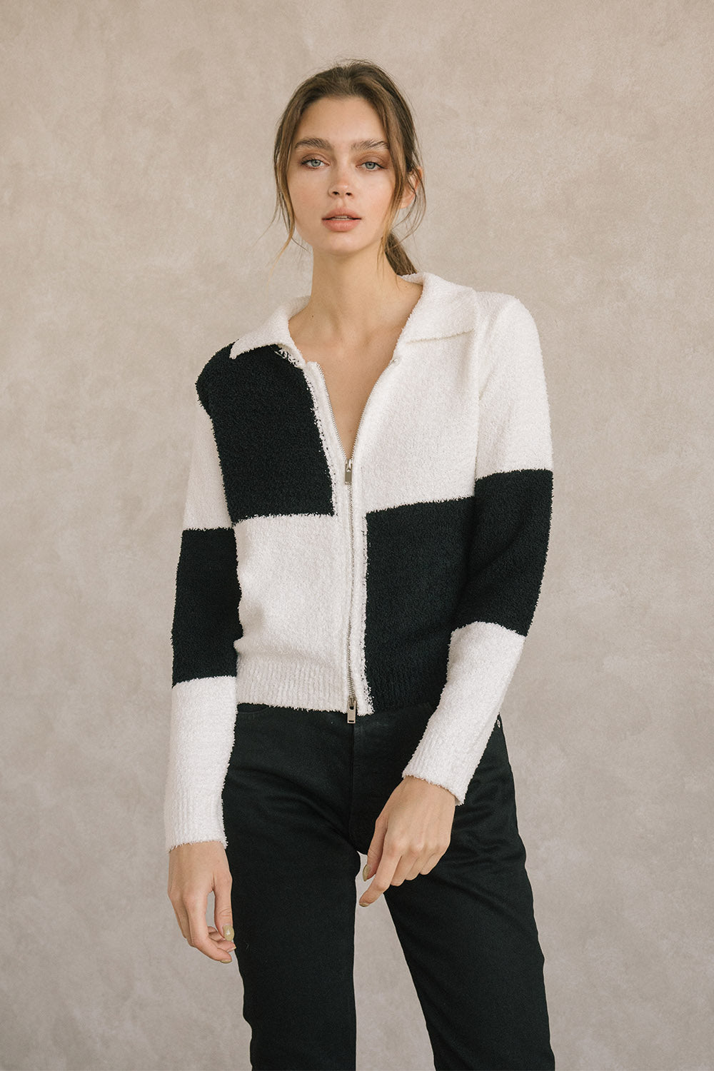 Woman wearing a black and white checkered zip-up sweater against a beige background