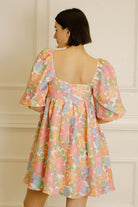 Back view of a woman wearing a floral dress against a neutral background
