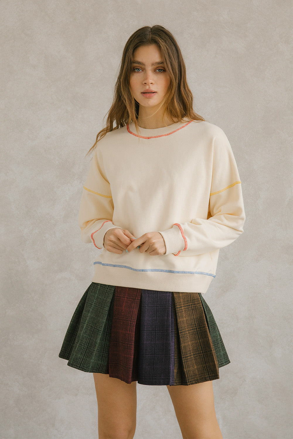 Cream pullover sweater with long sleeves and pleated plaid skirt. It has a crewneck and an oversized, loose fit. Sweet en Forme