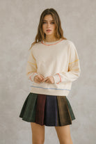 Cream pullover sweater with long sleeves and pleated plaid skirt. It has a crewneck and an oversized, loose fit. Sweet en Forme