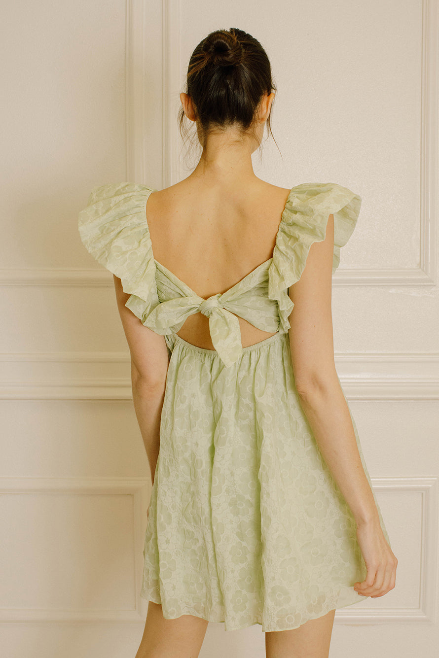 Back view of a woman in a green mini dress in a softly lit room.