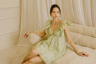 Woman in a green mini dress sitting on a beige sofa in a softly lit room.