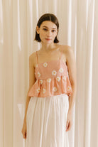 Woman wearing a pink floral top and white pants against a beige curtain background