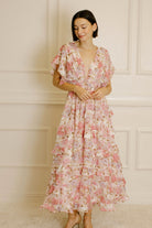 A woman wearing a pink and white floral maxi dress with short flutter sleeves and a V-neckline.