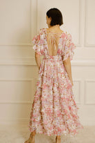 Woman wearing a pink and white floral dress with a backless design against a white paneled wall.