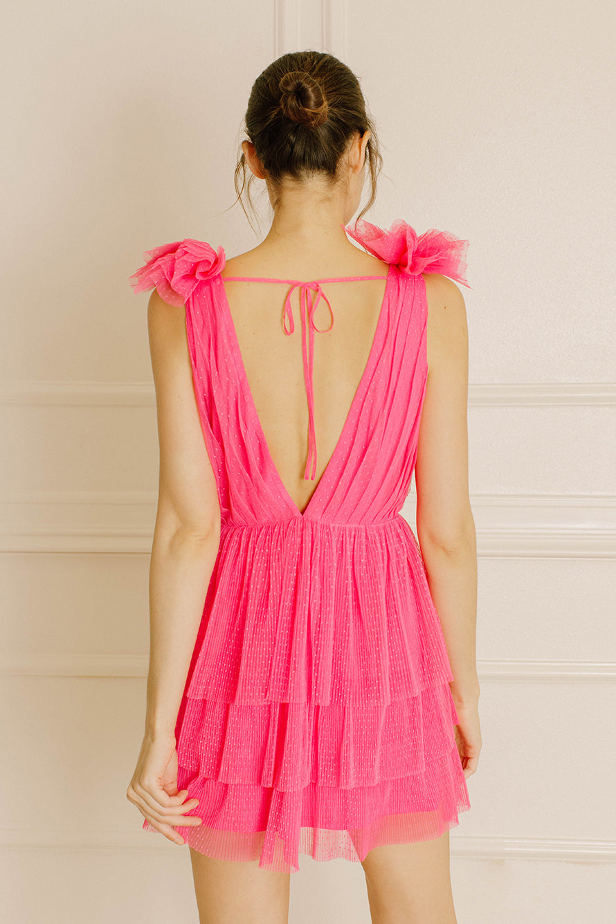 Back of a woman wearing a pink tulle dress with ruffled sleeves against a beige background