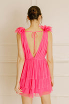 Back of a woman wearing a pink tulle dress with ruffled sleeves against a beige background