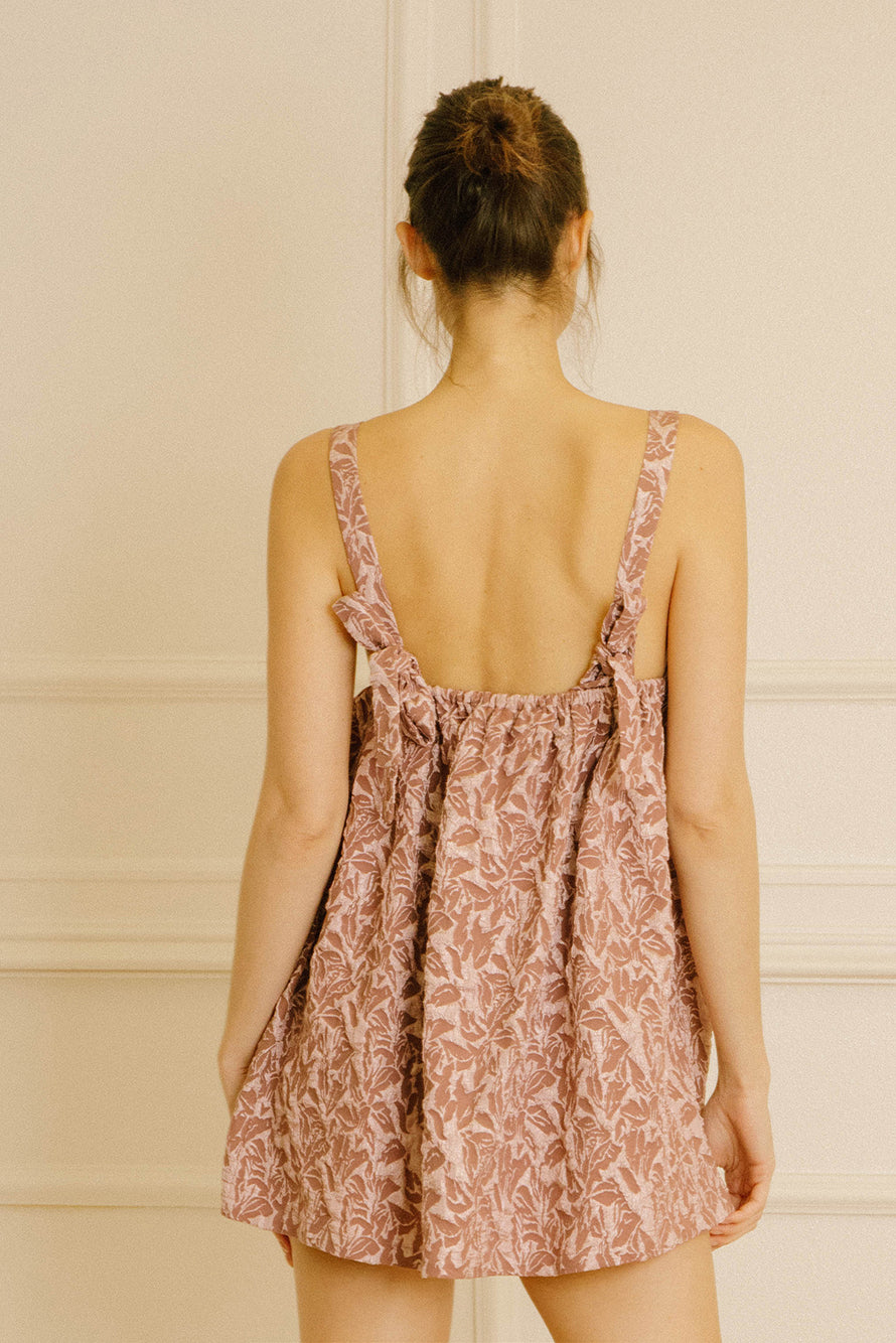 Back view of a woman wearing a mauve dress with embroidered leave against a neutral background