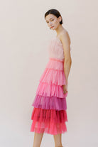 Side of a woman wearing a pink tulle tiered dress against a white background