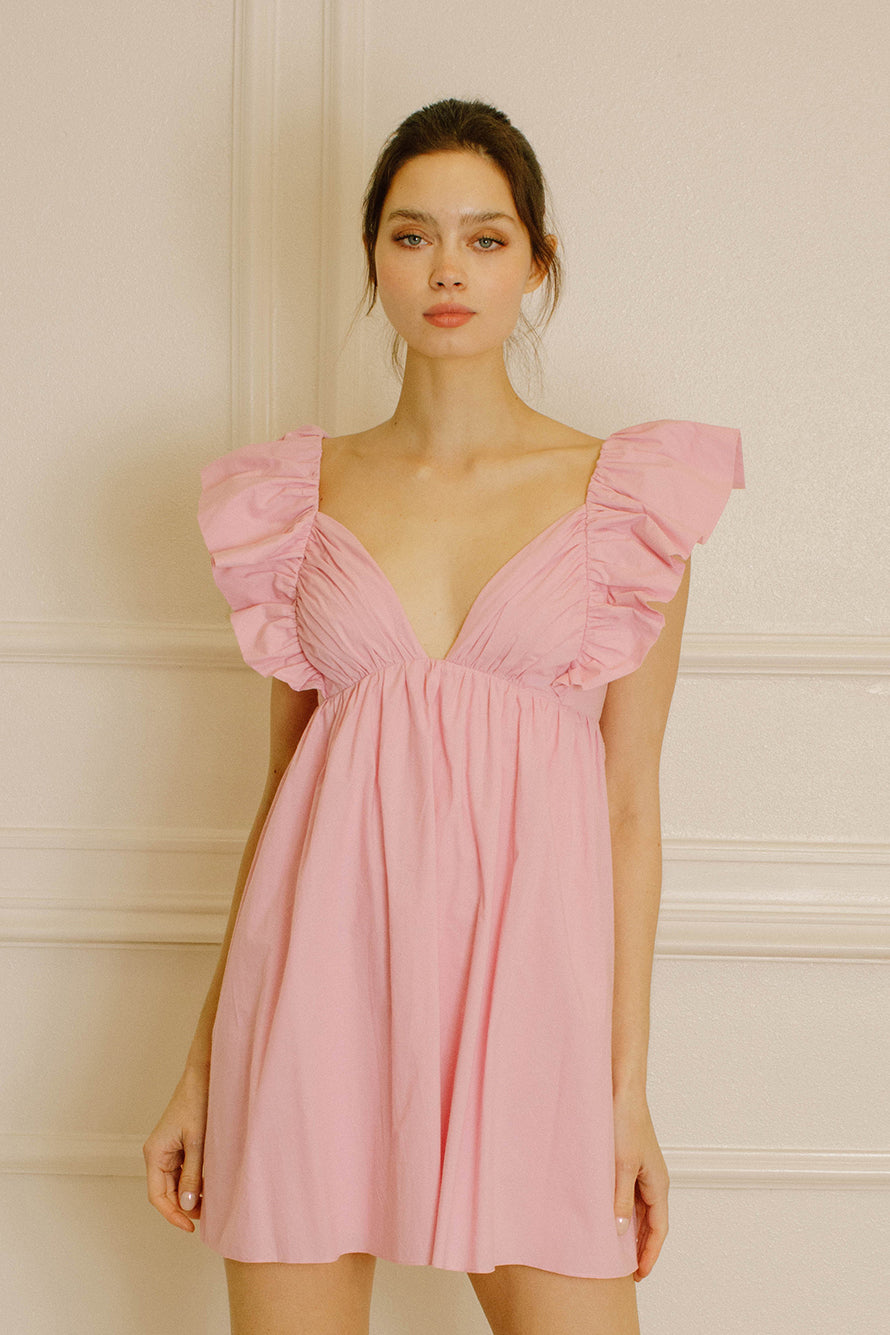 Woman wearing a pink dress with ruffled sleeves against a beige wall.