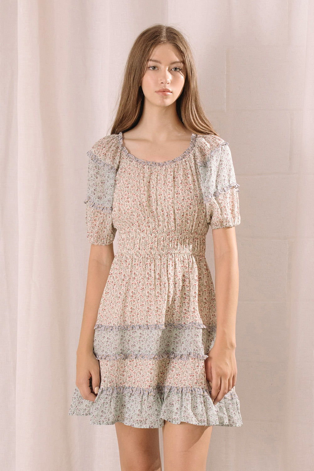 Woman wearing a blue and beige dress with floral pattern against a plain background