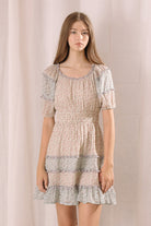 Woman wearing a blue and beige dress with floral pattern against a plain background