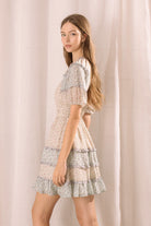Side view of a woman wearing a blue and beige dress with floral pattern against a plain background