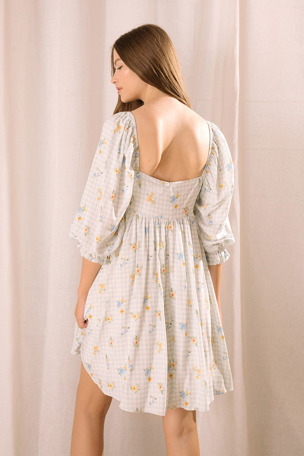 Back view of a model wearing a blue floral gingham  mini dress with a square neckline
