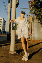 Woman wearing a blue floral gingham mini dress with a square neckline and beige sneakers.
