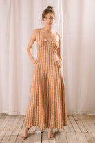 Woman wearing an orange checkered jumpsuit standing against a white curtain.