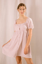 Woman wearing a pink dress with a heart pattern against a plain background