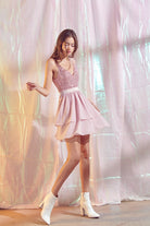 Woman in a blush shimmering party dress standing in front of a draped fabric background