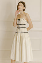 Woman wearing a cream midi dress with black trim against a neutral wall.