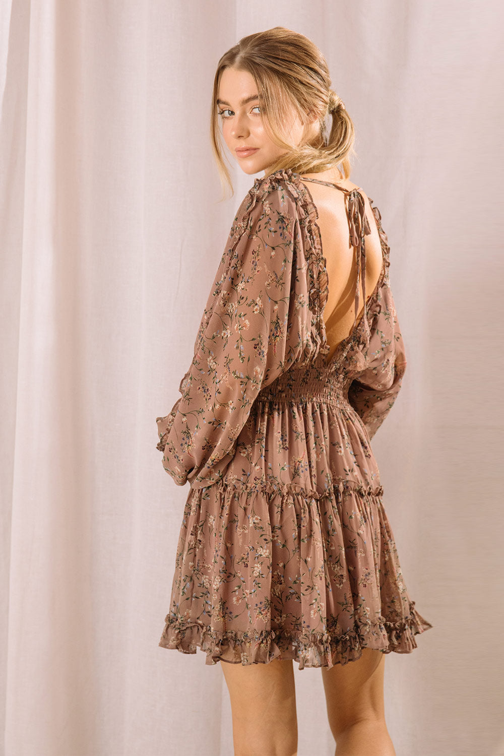 Back view of a woman wearing a brown dress with a floral pattern and an open back with self-tie straps