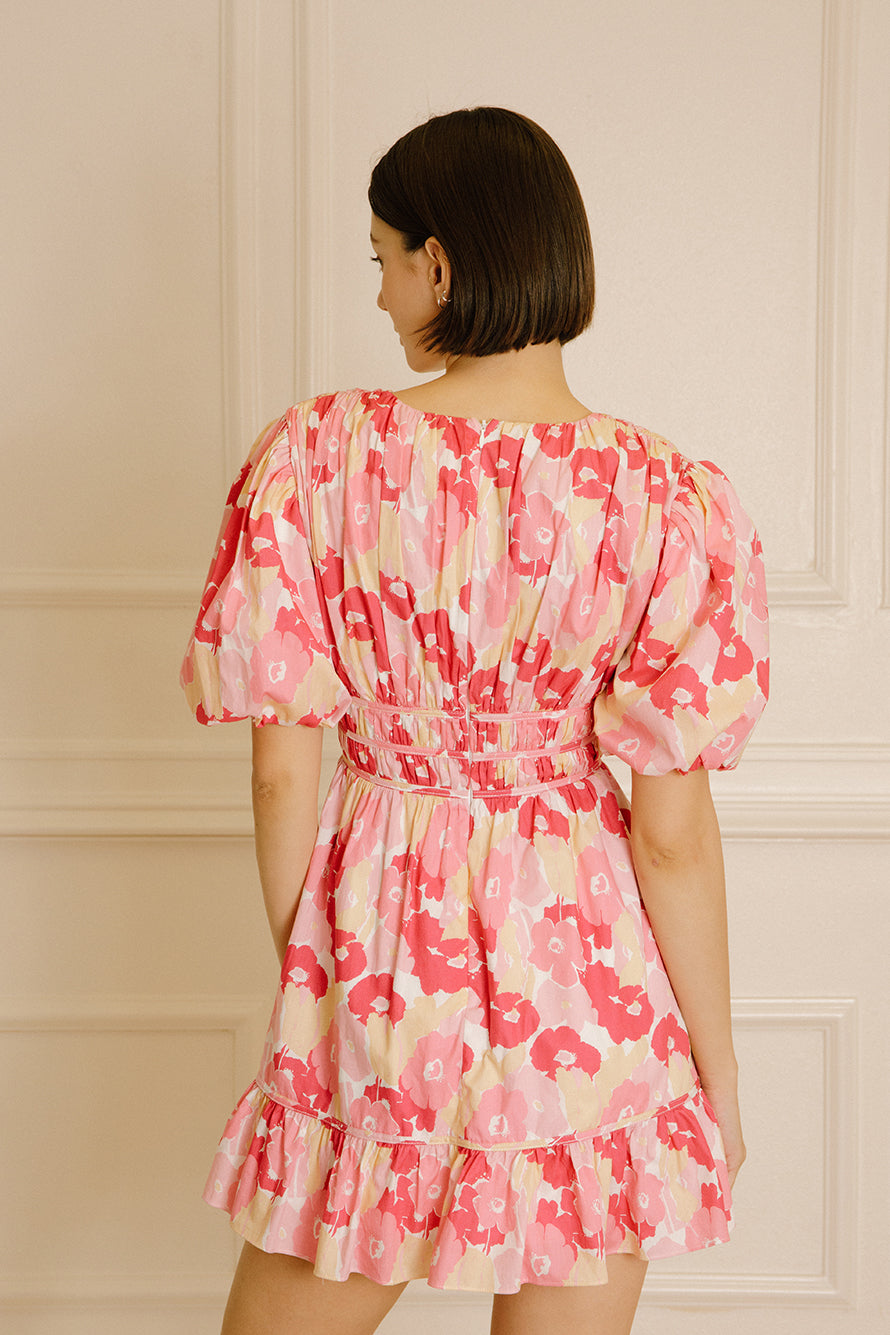 Back view of a woman wearing a pink and beige dress with a big floral pattern against a beige wall