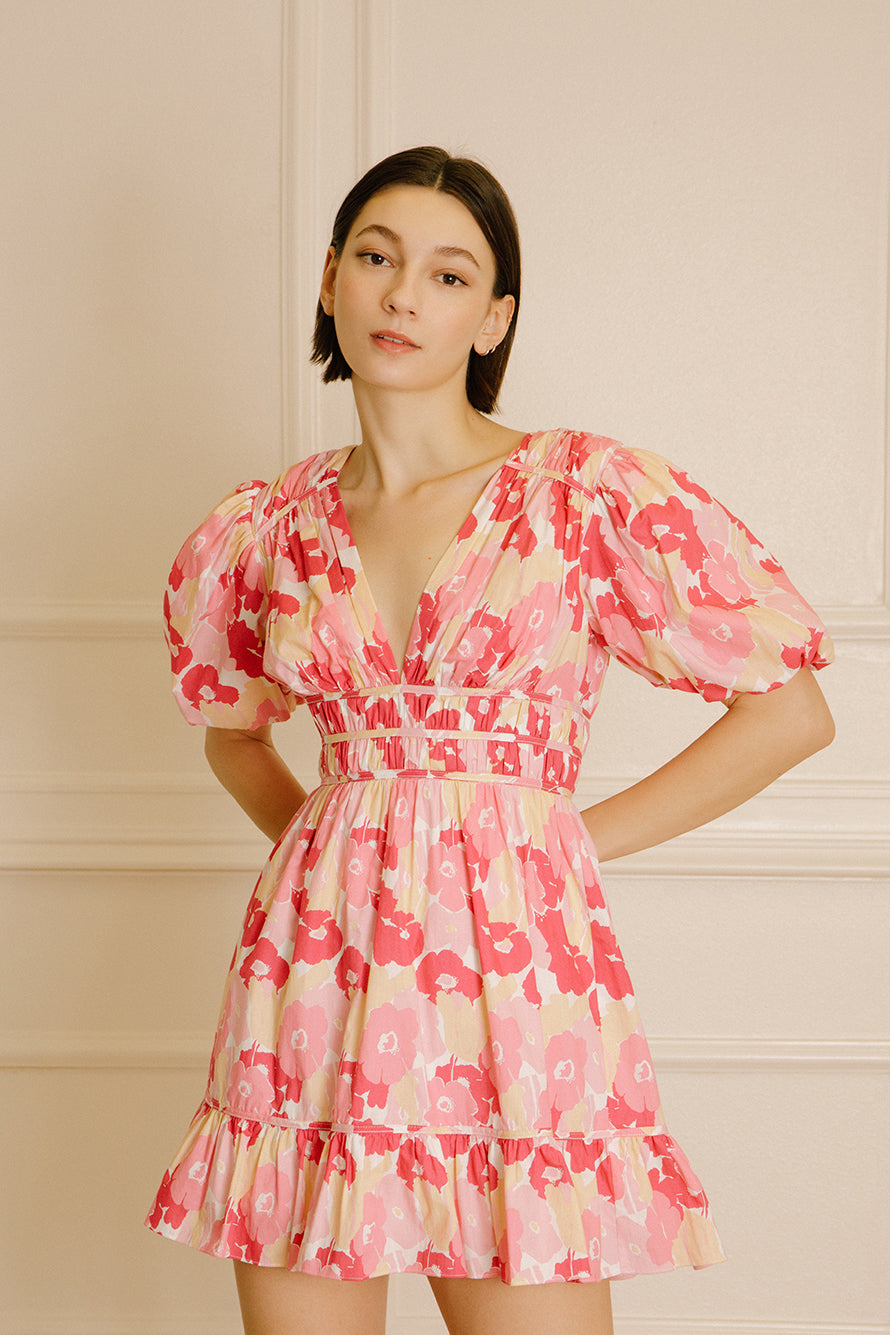 Woman wearing a pink and beige dress with a big floral pattern against a beige wall