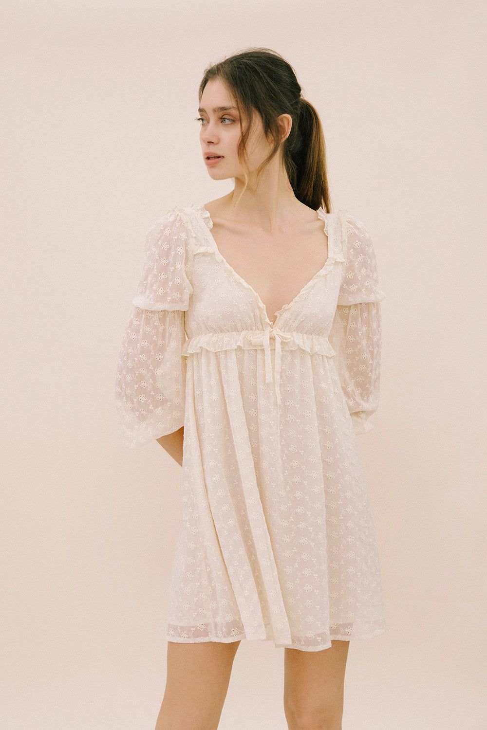 Woman wearing a sheer ivory dress against a plain background