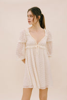 Woman wearing a sheer ivory dress against a plain background