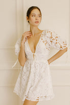 Woman wearing a white lace mini dress against a neutral wall
