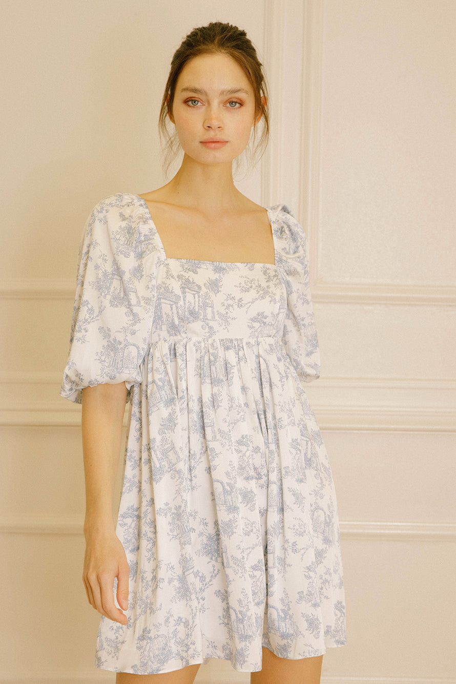 Woman wearing a white dress with a blue garden print against a neutral background