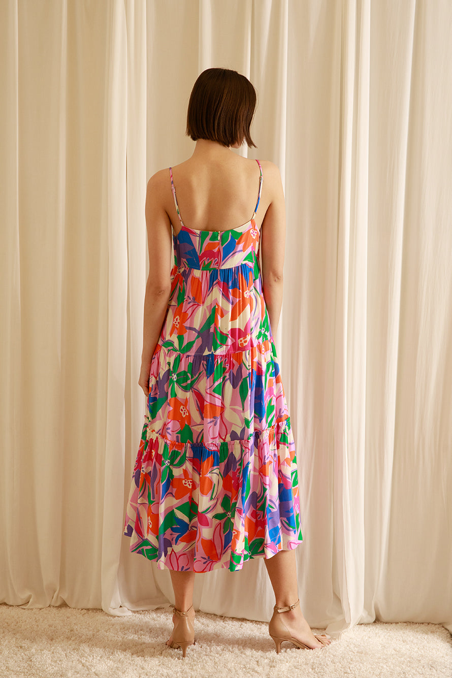 Back of a woman wearing a colorful floral dress standing against a beige curtain.