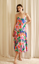 Woman wearing a colorful floral dress standing against a beige curtain.