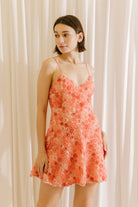 Woman wearing a coral floral dress against a white curtain background